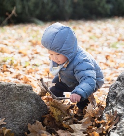 Un petit garçon s’amuse avec une branche et des feuilles mortes